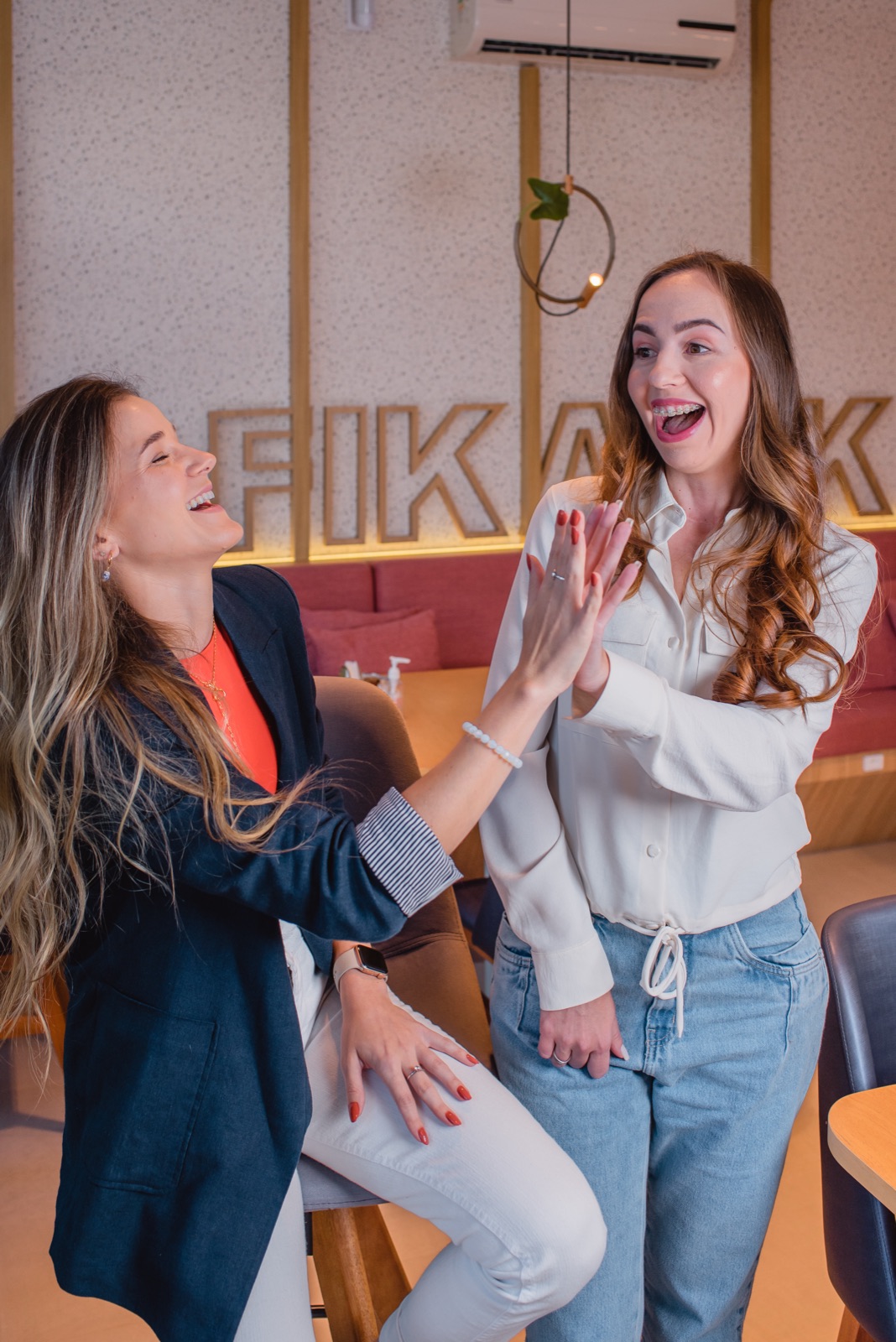 Kamila e Débora, fundadoras da Amaré Criativa, rindo juntas durante uma conversa de trabalho